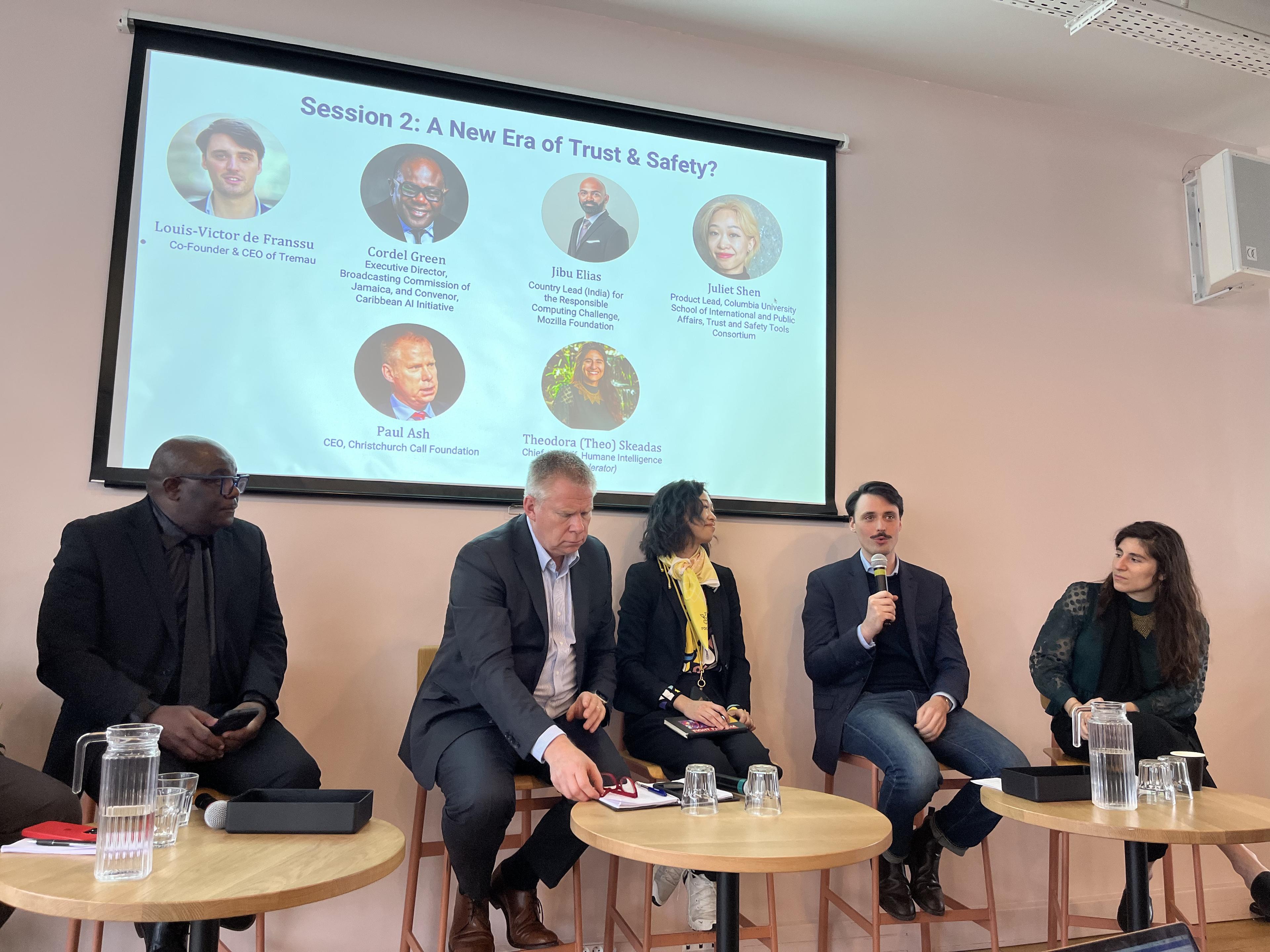 Panel discussion with five speakers seated under a presentation slide titled “Session 2: A New Era of Trust & Safety?”