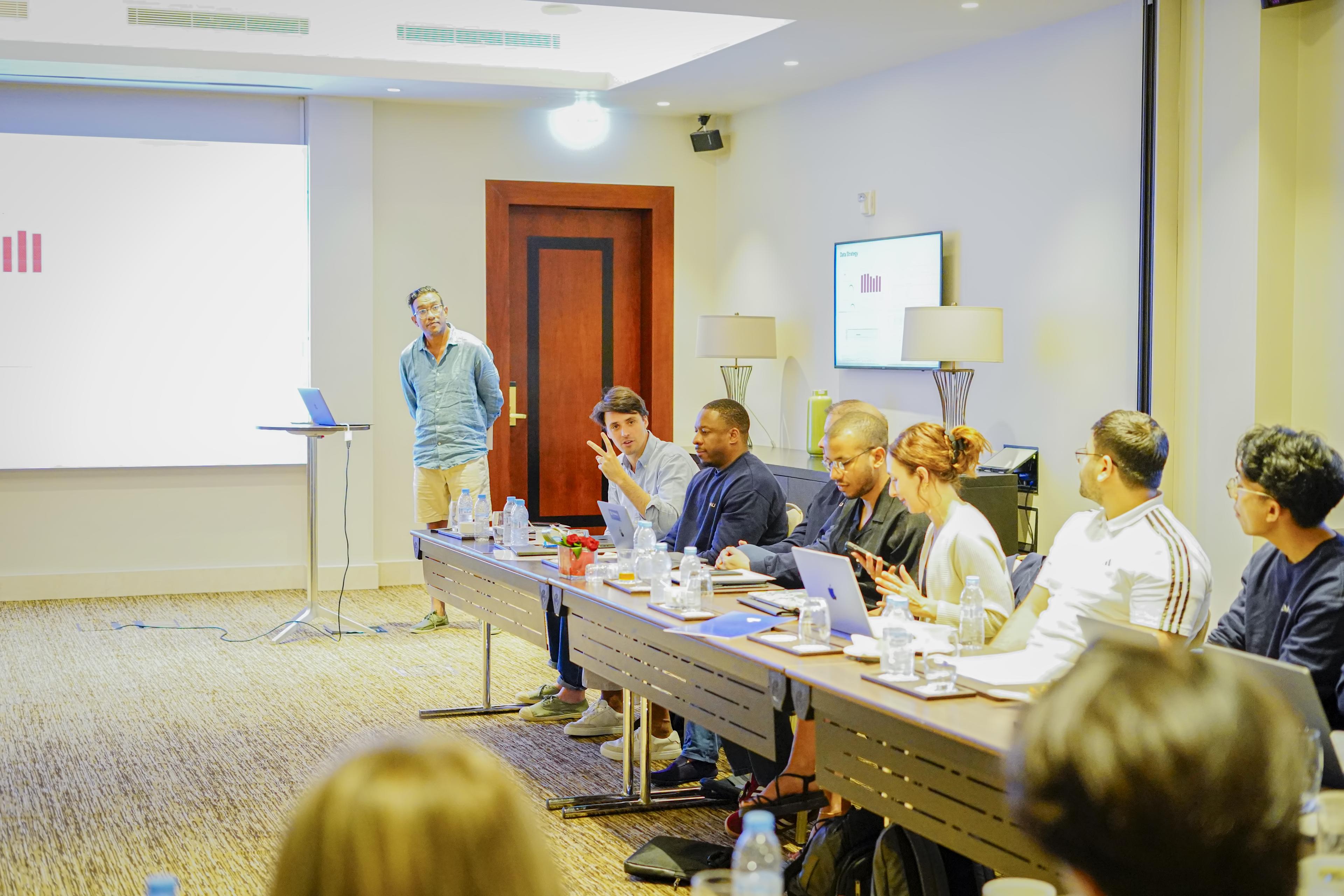 People seated at a conference table during a business meeting with a presentation screen.