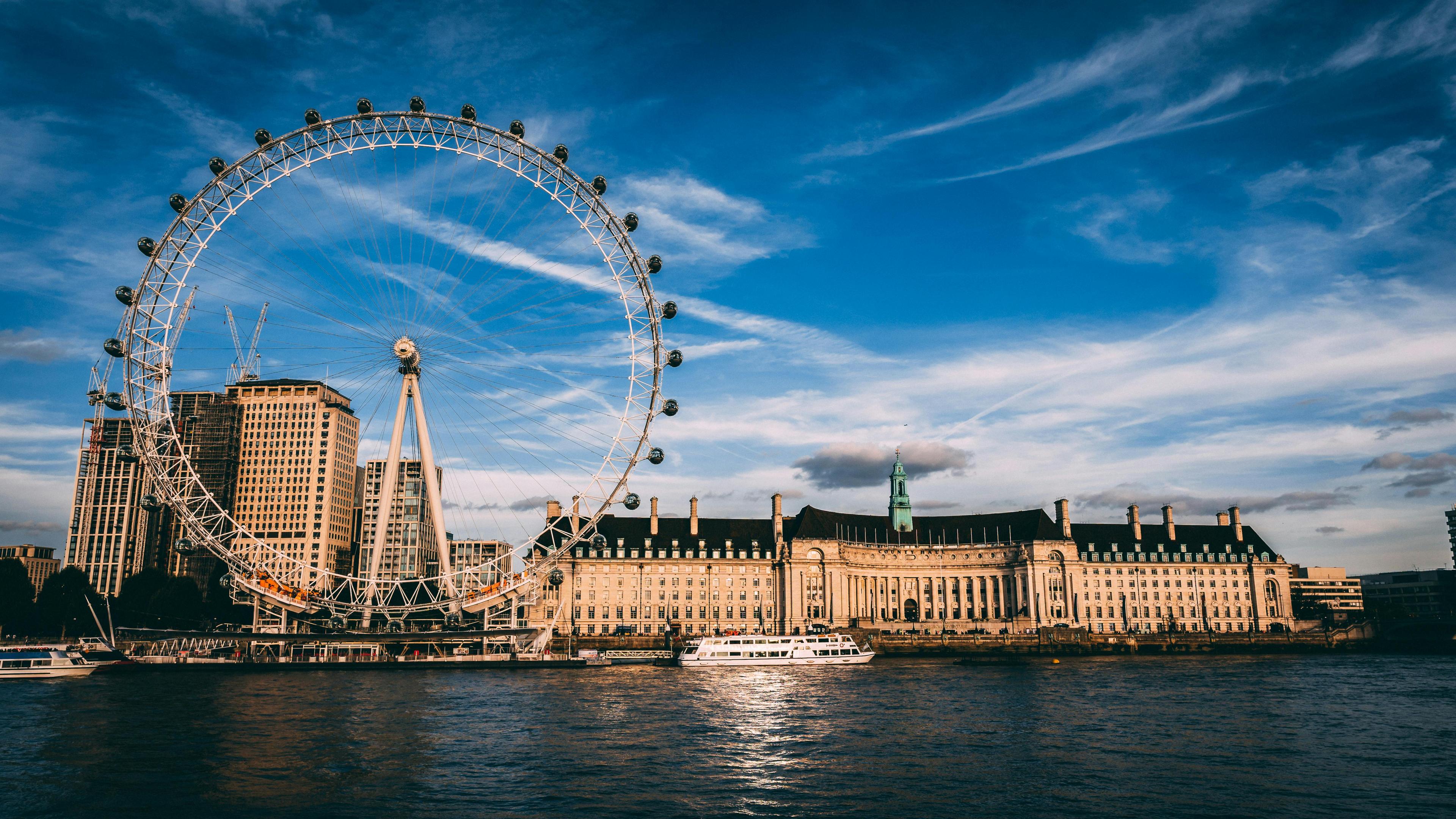 London Eye ferris wheel beside the Thames River under a blue sky.